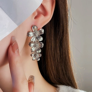 Macro shot of silver vintage metal flower tassel earrings worn on model's ear