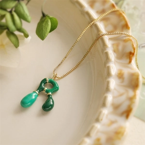Dettaglio di una catena dorata con pendente in smalto verde su un piatto in ceramica decorativa