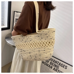 Detail of a large woven straw tote bag in cream and black on a model's shoulder