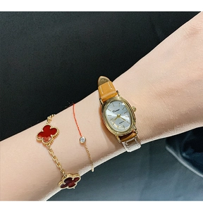 Elegant oval gold watch with brown leather strap and minimalist dial worn on wrist