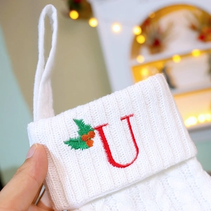 White knitted Christmas stocking with red embroidered letter U and holly berry decoration
