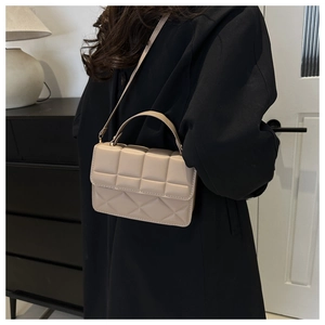 Beige quilted shoulder bag with top handle and strap styled on a black coat