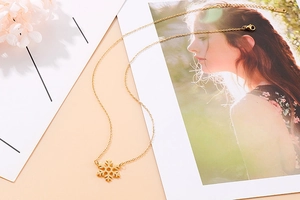 Artistic display of a gold snowflake necklace on warm beige background with dried flowers