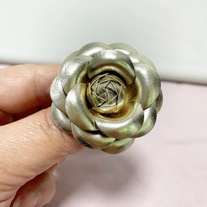 Close-up of golden PU leather camellia flower brooch with detailed metallic texture