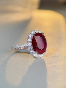 Macro shot of an oval red ruby gemstone ring with a white diamond halo and silver band