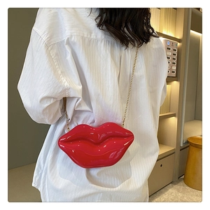 Red lip-shaped acrylic crossbody bag with gold chain shown on model in a white shirt