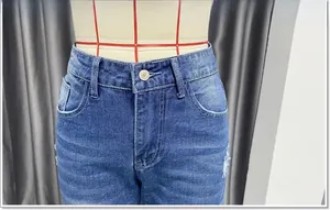 Detailweergave van de blauwe high-waist jeans met metalen knoop en gewassen denim textuur