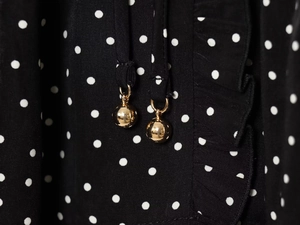Detail of ruffled black polka dot fabric with elegant gold spherical pendant drawstring