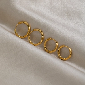 Minimalist gold-plated stainless steel twisted hoop earrings on soft silk fabric