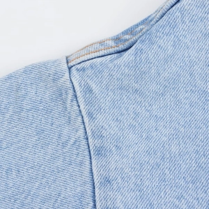 Detailed close-up of double orange stitching on light blue denim fabric shoulder seam