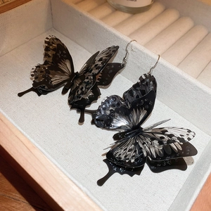 Dark style acrylic butterfly hook earrings with layered wings on a beige jewelry box