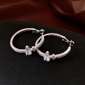 Close-up of silver hoop earrings with clear zircons and Saturn-style charms on black base