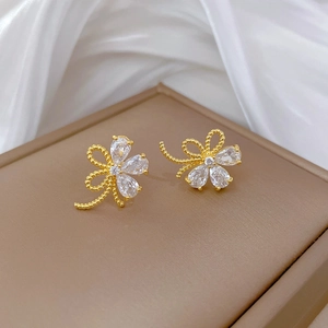 Nahaufnahme goldener Blumen-Ohrstecker mit weißen Zirkonia auf weißem Seidenhintergrund