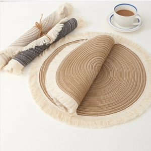 Detail of round woven placemats with fringe edges in brown, beige, and grey cotton