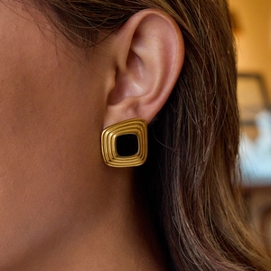 Gros plan d'une boucle d'oreille carrée en acier doré et résine noire sur modèle