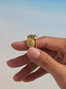 Detail of 18K gold-plated rings set with green zircon and sun relief on a finger