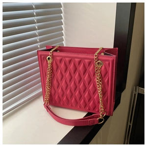 Detail of rose red quilted tote bag with gold chain strap in natural sunlight