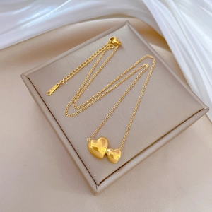 Minimalist double heart pendant necklace in gold finish on elegant white silk fabric