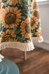 Detailed macro view of woven sunflower tapestry tablecloth with elegant beige fringe edges