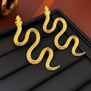Exaggerated golden snake earrings with black diamond eyes and engraved scales