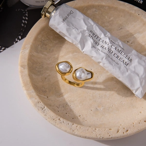 Detail of baroque pearl open ring with gold finish on a minimalist textured surface