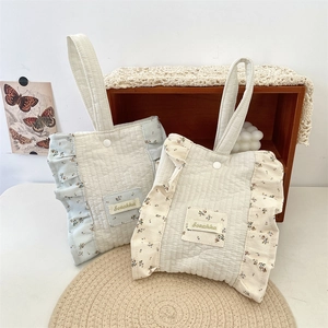 Detailed close-up of floral quilted cotton wrist bag with ruffled edges in cream and blue