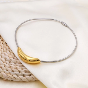 Macro view of gold curved tube pendant on silver snake chain over silk background