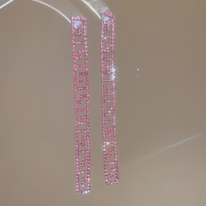 Dettaglio di orecchini con strass rosa, motivo a greca e lunghe nappe pendenti