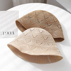 Hollow knit bucket hats in beige and khaki with wavy crochet texture on white table