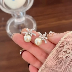 Macro shot of elegant silver flower pearl earrings held by hand with cubic zirconia
