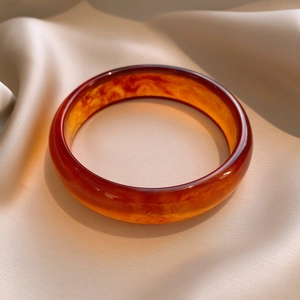 Close-up of polished amber resin bangle with natural texture on beige silk background