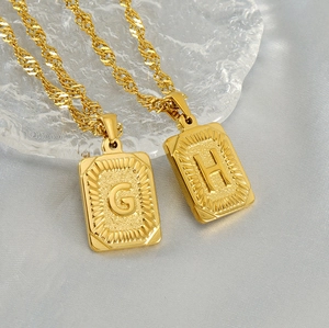 Close-up of 18K gold-plated square pendant necklaces with engraved letters G and H