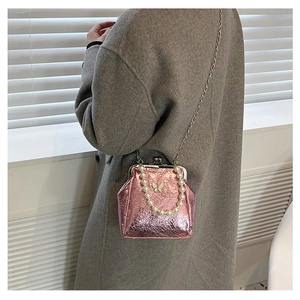 Pink metallic crossbody bag with pearl handle and butterfly clasp shown on gray coat