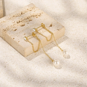 Macro detail of long gold tassel chain pearl earrings displayed on a beige stone surface