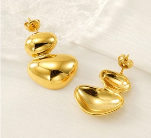 Détail de boucles d'oreilles géométriques dorées posées sur un fond de soie blanche élégant