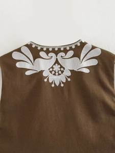 Close-up of white floral embroidery details on the neckline of a dark brown vest