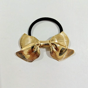 Detail of golden metal bow hair tie with crinkled texture and black elastic band