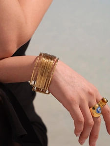 Detail of layered gold-plated cuff bracelet and chunky ring with blue heart inlay