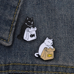Detail of two cute alloy cat badges with black and white fish bags on denim fabric