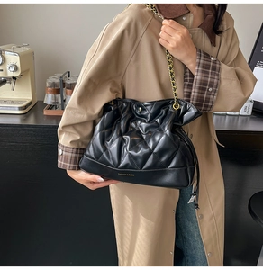 Quilted black leather bucket bag with gold chain strap shown in a modern cafe setting