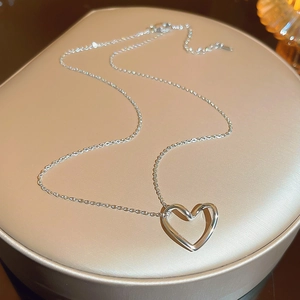 Macro detail of minimalist silver heart pendant on a fine chain over metallic display