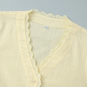 Détail du col en V avec broderie festonnée et bouton sur chemise jaune en lin