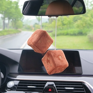 Macro view of plush brown dice car charms with embroidered hearts hanging in a vehicle