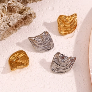 Macro detail of irregular gold and silver shell earrings on wet textured background