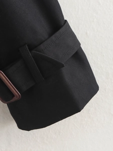 Gros plan sur la manche du trench noir avec sangle décorative en similicuir marron à boucle