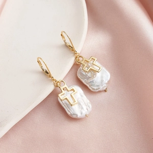 Golden cross earrings with hanging irregular white freshwater pearls on satin fabric