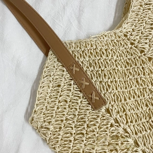 Detail of hand-woven straw tote bag with brown faux leather strap and X-stitch sewing