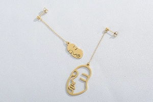 Détail de boucles d'oreilles dorées asymétriques avec lignes de visage abstraites