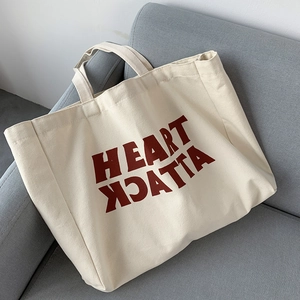 Close-up of cream canvas tote bag with red Heart Attack typography on grey sofa
