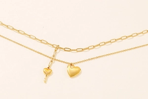 Detailed shot of double-layer gold heart and key pendants on paperclip chain necklace